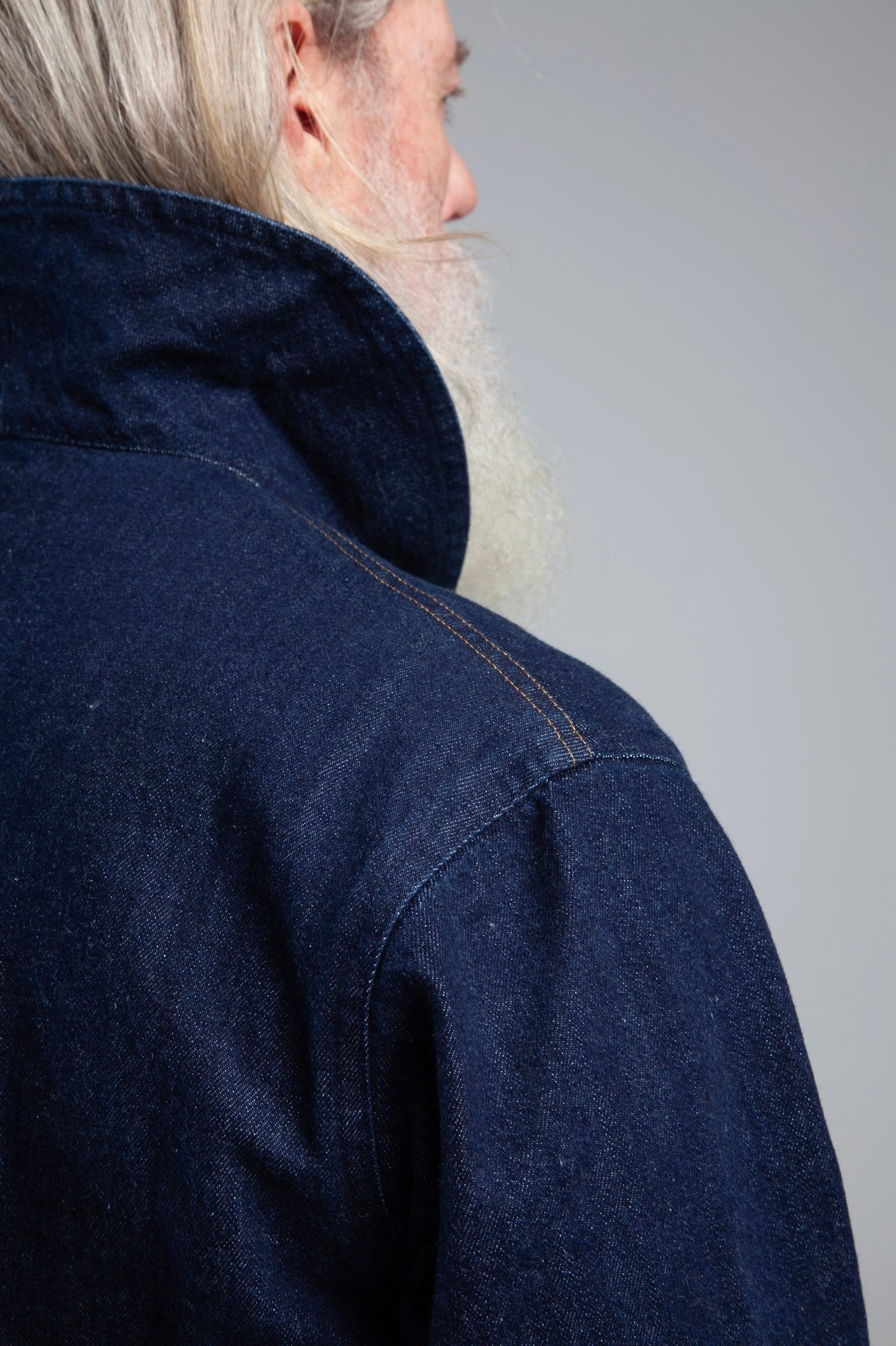Person wearing a dark blue denim jacket against a gray background